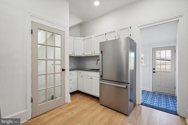 kitchen featuring decorative backsplash, light wood-type flooring, white cabinetry, and stainless steel refrigerator