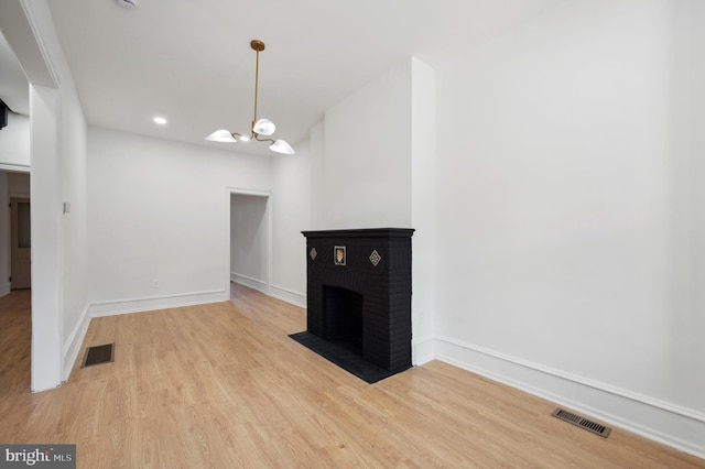 unfurnished living room featuring a fireplace, an inviting chandelier, and light wood-type flooring