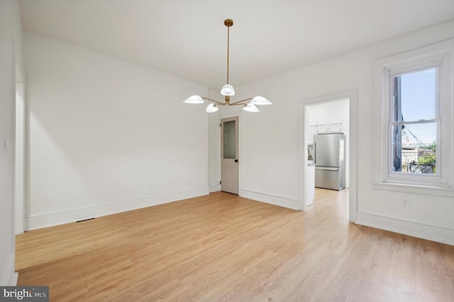 empty room with light hardwood / wood-style floors and an inviting chandelier