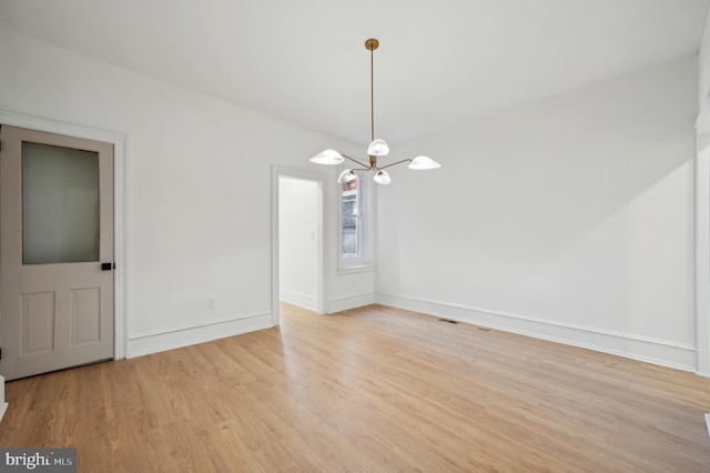 spare room featuring light hardwood / wood-style floors and a notable chandelier