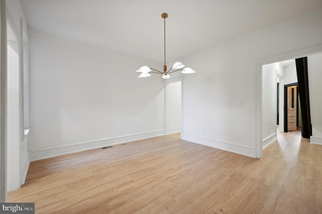 spare room featuring light wood-type flooring and a notable chandelier