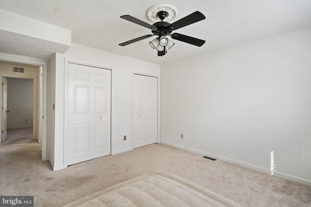 unfurnished bedroom featuring two closets, a textured ceiling, light colored carpet, and ceiling fan