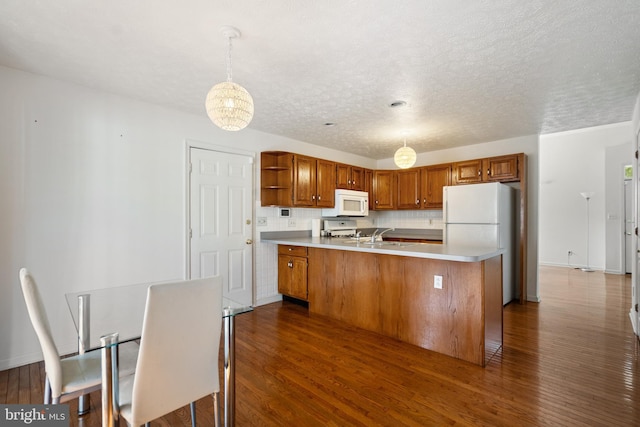 kitchen with white appliances, dark hardwood / wood-style floors, a textured ceiling, tasteful backsplash, and decorative light fixtures