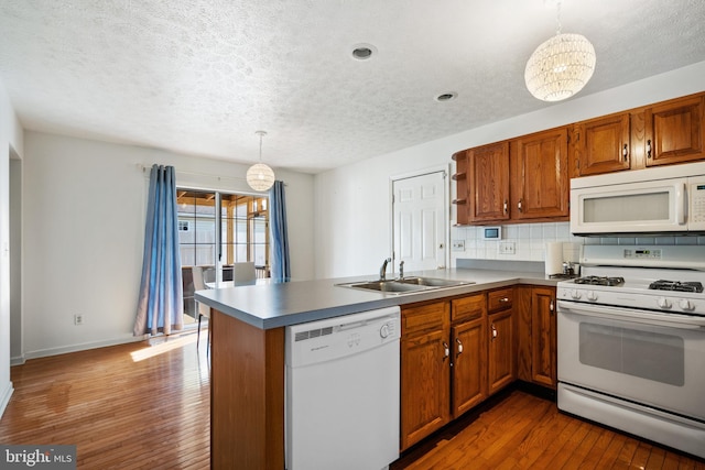 kitchen featuring sink, hanging light fixtures, dark hardwood / wood-style flooring, kitchen peninsula, and white appliances