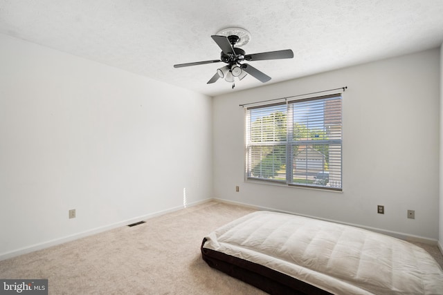 bedroom with ceiling fan, light colored carpet, and a textured ceiling