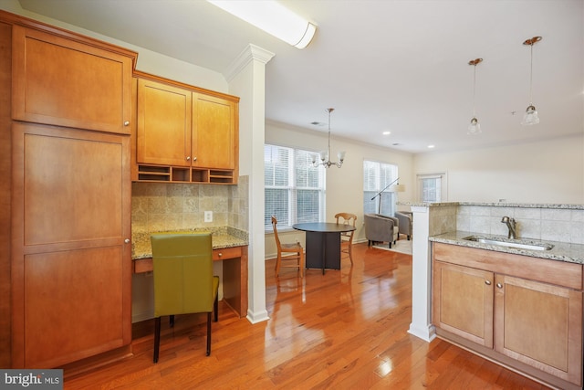 kitchen featuring sink, tasteful backsplash, light stone counters, pendant lighting, and hardwood / wood-style flooring