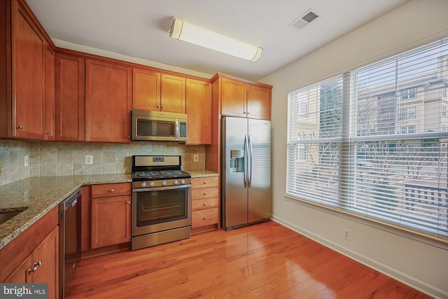 kitchen featuring light stone countertops, appliances with stainless steel finishes, light wood-type flooring, and tasteful backsplash