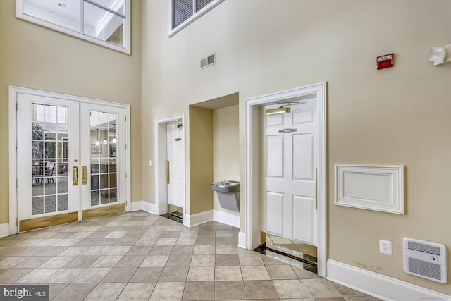 tiled entryway with heating unit, french doors, and a towering ceiling