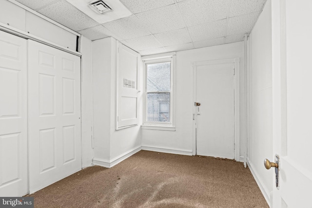 unfurnished bedroom with a closet, a drop ceiling, and carpet floors