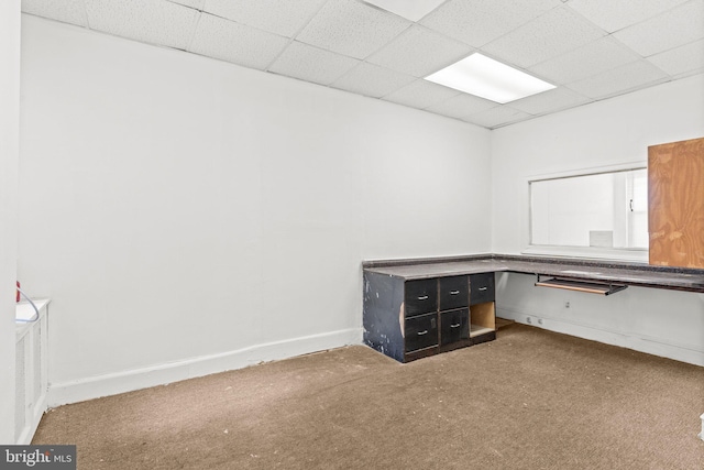 unfurnished office featuring carpet flooring, a drop ceiling, and built in desk