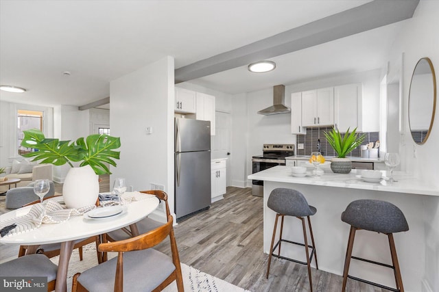 kitchen with appliances with stainless steel finishes, light wood-type flooring, white cabinetry, and wall chimney exhaust hood