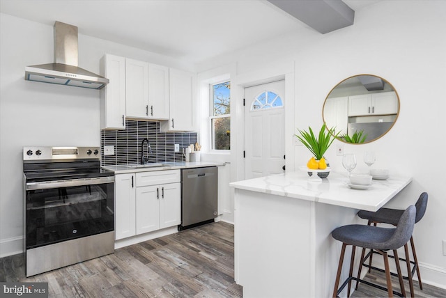 kitchen with appliances with stainless steel finishes, wall chimney exhaust hood, dark wood-type flooring, sink, and white cabinetry