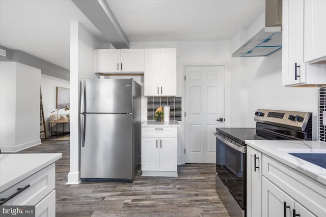 kitchen with dark wood-type flooring, wall chimney range hood, appliances with stainless steel finishes, tasteful backsplash, and white cabinetry