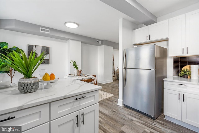 kitchen featuring stainless steel fridge, light wood-type flooring, white cabinetry, and light stone counters