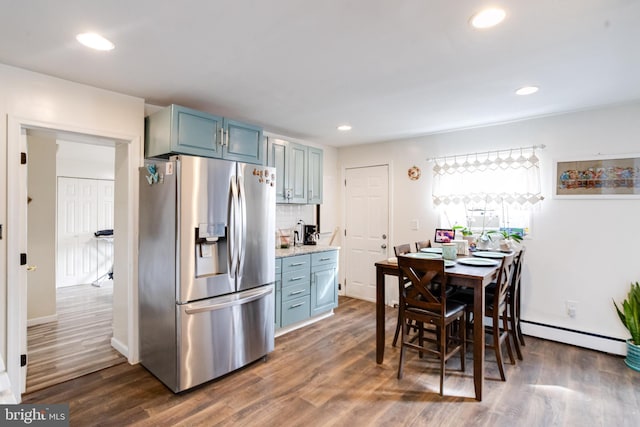 kitchen with blue cabinets, stainless steel fridge with ice dispenser, dark hardwood / wood-style flooring, baseboard heating, and tasteful backsplash