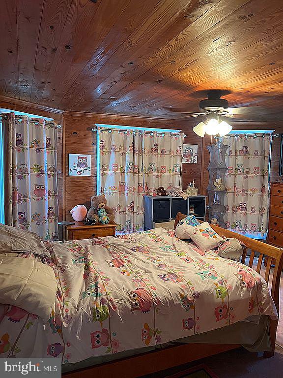 bedroom with ceiling fan, wooden ceiling, and wood walls