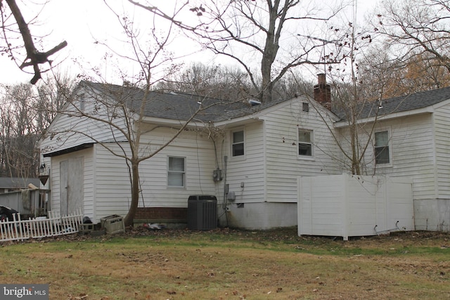 rear view of house with central air condition unit and a yard