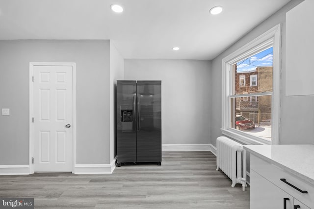 interior space featuring stainless steel refrigerator with ice dispenser, radiator, white cabinets, and light wood-type flooring