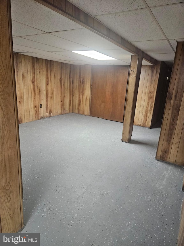 basement with a drop ceiling and wood walls