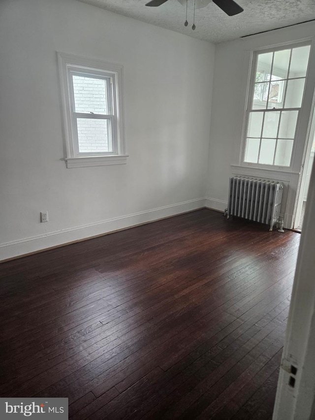 empty room with a textured ceiling, ceiling fan, radiator heating unit, and dark wood-type flooring