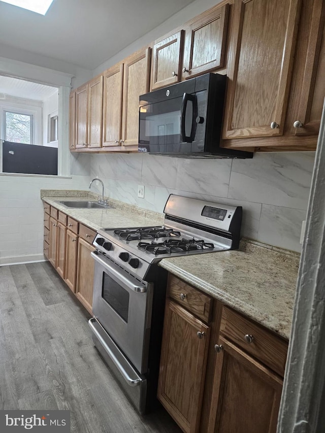 kitchen with gas stove, backsplash, sink, and light hardwood / wood-style flooring