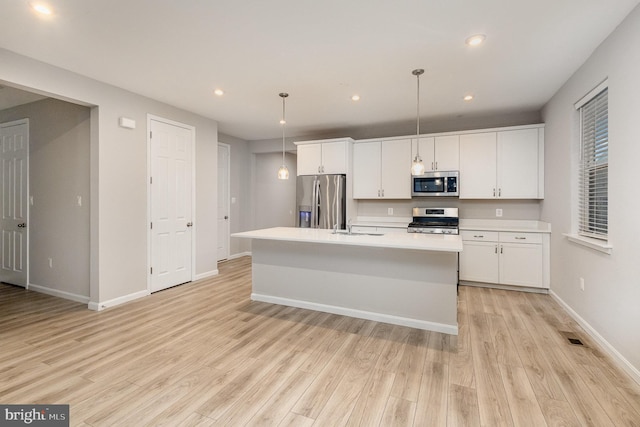 kitchen with appliances with stainless steel finishes, a center island with sink, light hardwood / wood-style flooring, and decorative light fixtures