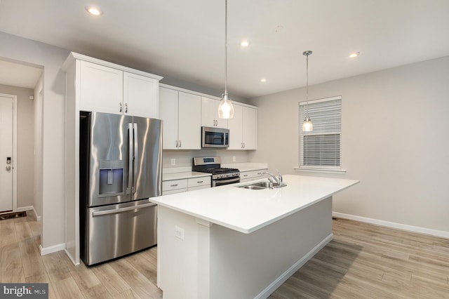 kitchen with appliances with stainless steel finishes, sink, pendant lighting, white cabinetry, and an island with sink