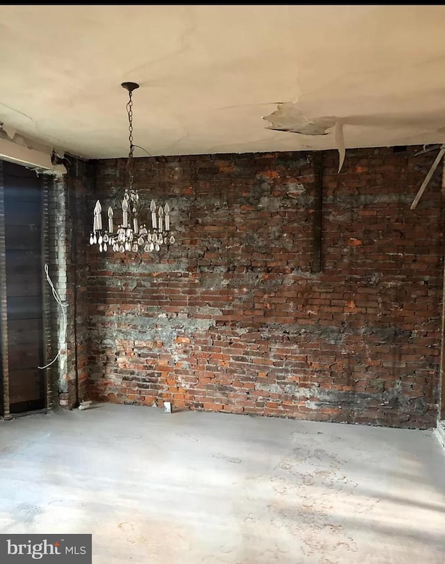 unfurnished dining area with an inviting chandelier, brick wall, and concrete floors