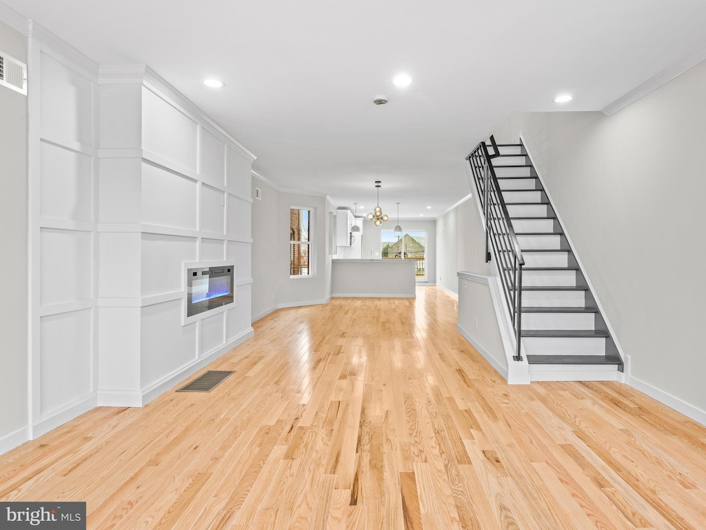 unfurnished living room featuring heating unit, crown molding, a chandelier, and light wood-type flooring