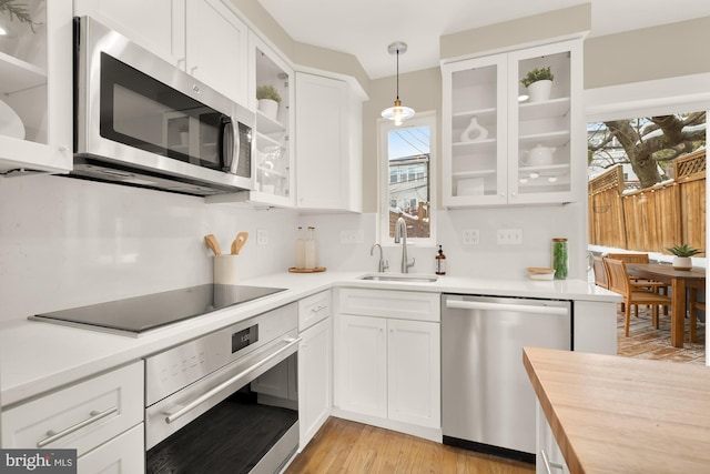 kitchen featuring a wealth of natural light, white cabinetry, sink, stainless steel appliances, and decorative light fixtures