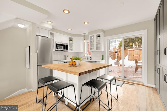 kitchen featuring butcher block counters, light hardwood / wood-style flooring, white cabinetry, a breakfast bar area, and stainless steel appliances