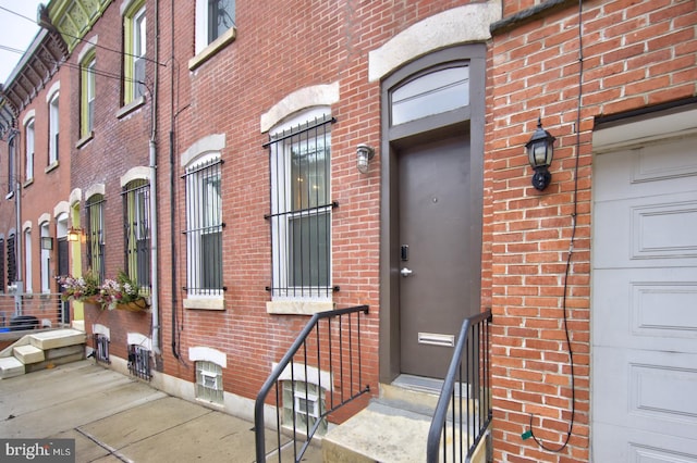 view of exterior entry featuring a garage and brick siding