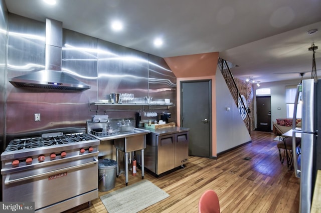 kitchen with stainless steel appliances, wall chimney exhaust hood, modern cabinets, and light wood-style floors