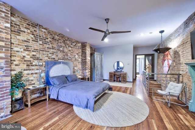 bedroom featuring a ceiling fan, brick wall, and wood finished floors