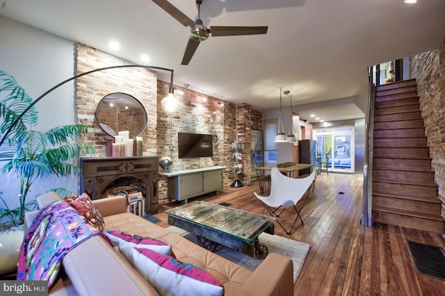 living area with a fireplace, wood-type flooring, visible vents, stairway, and ceiling fan