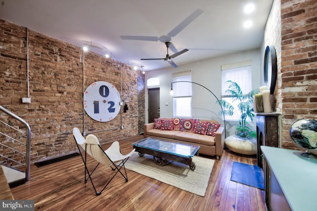 living area featuring brick wall, wood-type flooring, and a ceiling fan