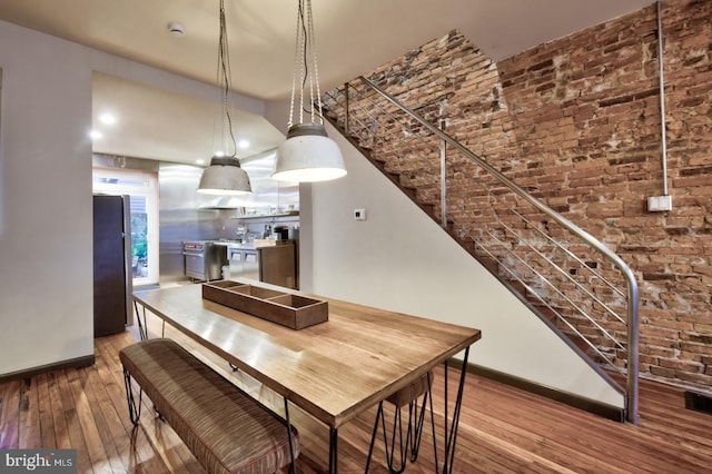 dining room with brick wall, baseboards, hardwood / wood-style floors, and stairs