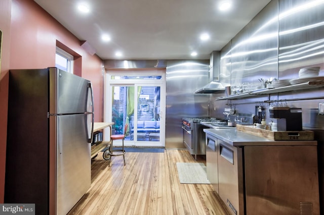 kitchen with light wood-style flooring, recessed lighting, freestanding refrigerator, wall chimney exhaust hood, and dark countertops