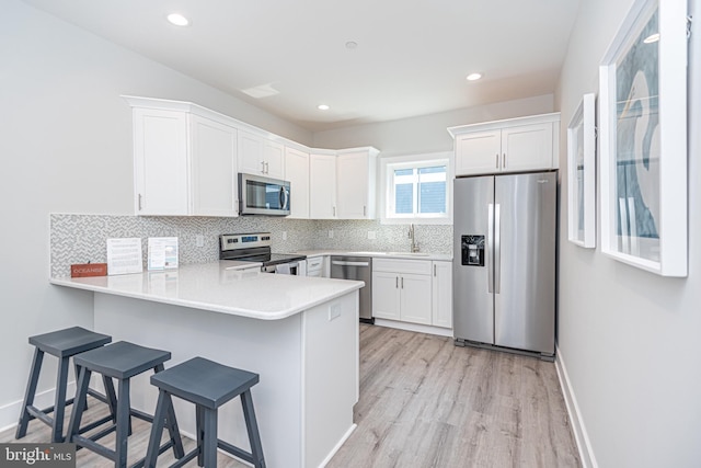 kitchen with kitchen peninsula, appliances with stainless steel finishes, light hardwood / wood-style floors, white cabinetry, and a breakfast bar area