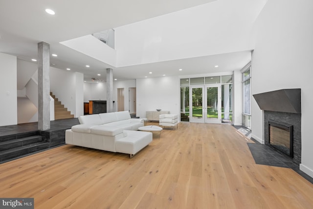 living area with a fireplace with flush hearth, hardwood / wood-style floors, stairs, floor to ceiling windows, and recessed lighting