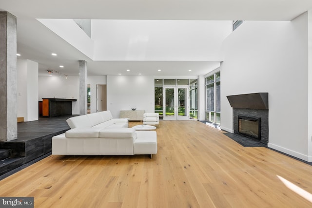 living area with a stone fireplace, light wood-style flooring, recessed lighting, baseboards, and a wall of windows