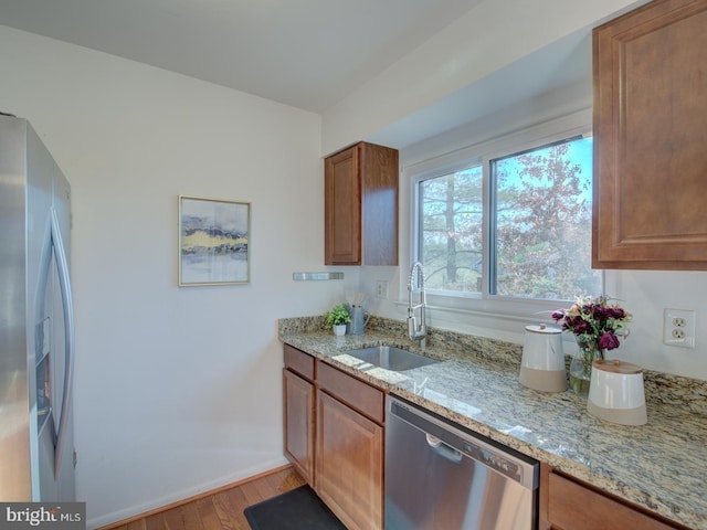 kitchen with light stone countertops, sink, stainless steel appliances, and light wood-type flooring