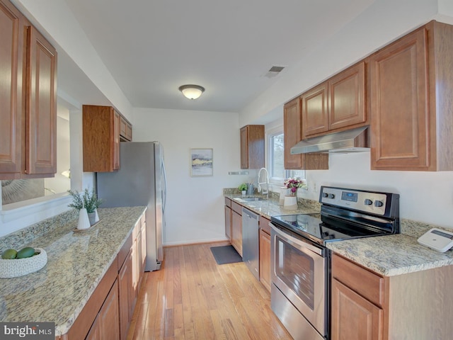 kitchen featuring appliances with stainless steel finishes, light hardwood / wood-style floors, light stone counters, and sink