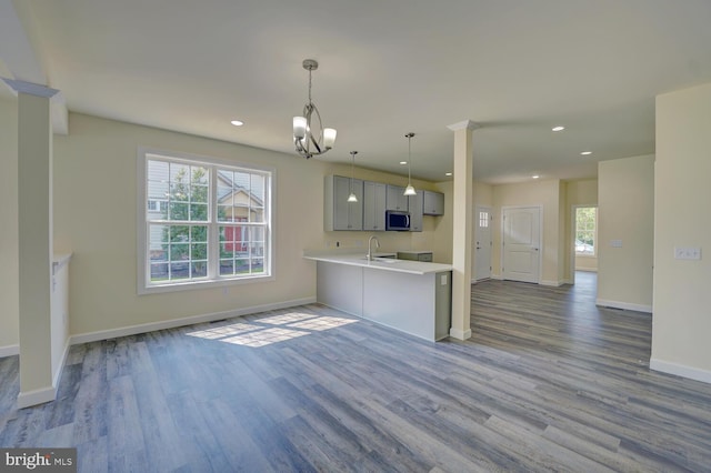 kitchen featuring gray cabinetry, an inviting chandelier, hanging light fixtures, light hardwood / wood-style flooring, and kitchen peninsula