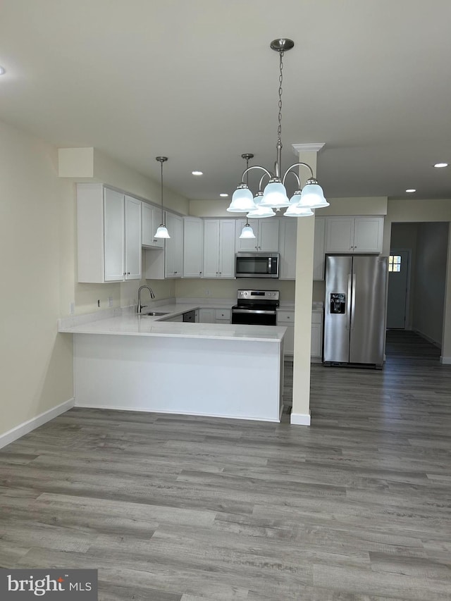 kitchen featuring white cabinets, appliances with stainless steel finishes, light wood-type flooring, and pendant lighting