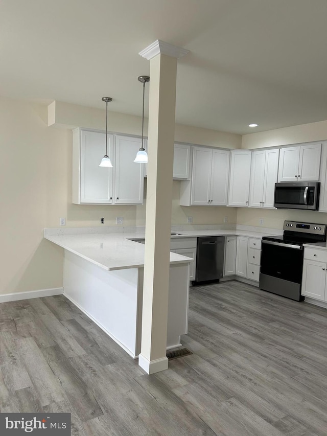 kitchen with appliances with stainless steel finishes, light hardwood / wood-style flooring, white cabinetry, and decorative light fixtures