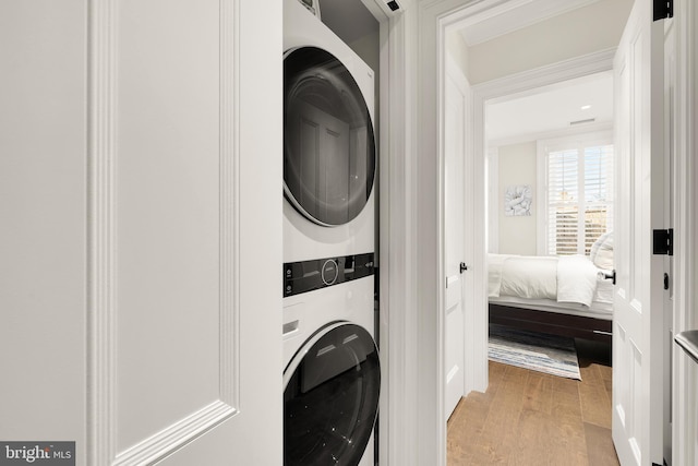 washroom with light hardwood / wood-style floors and stacked washer / drying machine