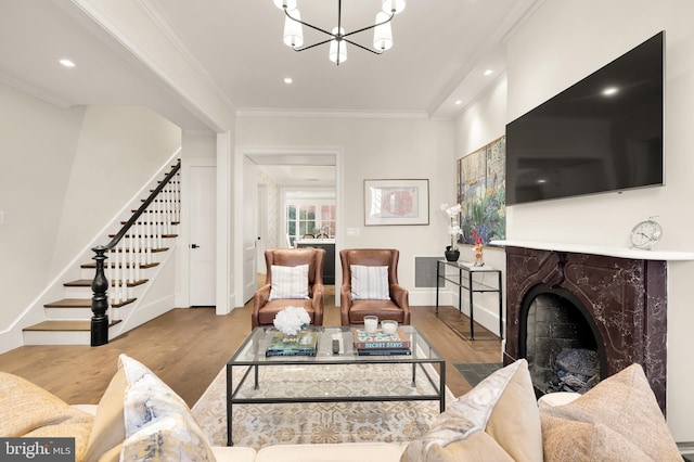 living room with a premium fireplace, a chandelier, light wood-type flooring, and ornamental molding