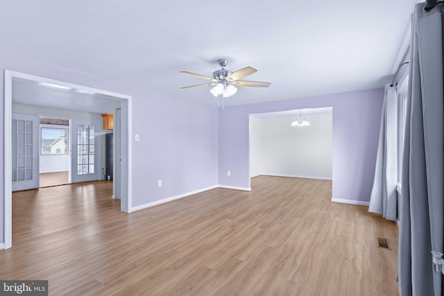 empty room with light wood-type flooring and ceiling fan with notable chandelier