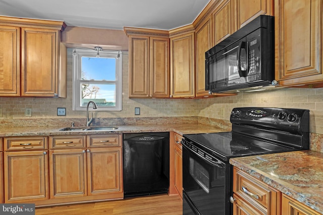 kitchen featuring black appliances, light stone countertops, sink, light hardwood / wood-style flooring, and backsplash